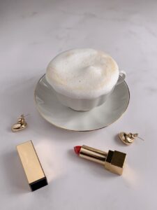 French Beauty 
foamy coffee in white cup beside golden earrings and red lipstick
