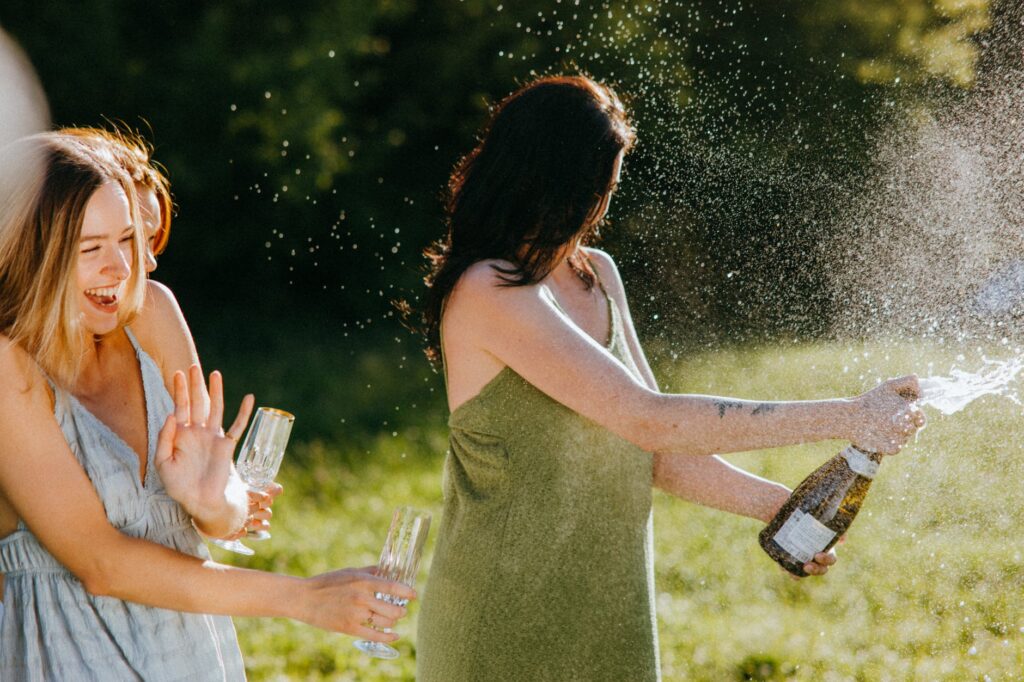 Chic Style Collective | 6 Simple and Elegant Summer Garden Party Ideas 2024 garden party ideas a woman in a green dress popping a champagne bottle